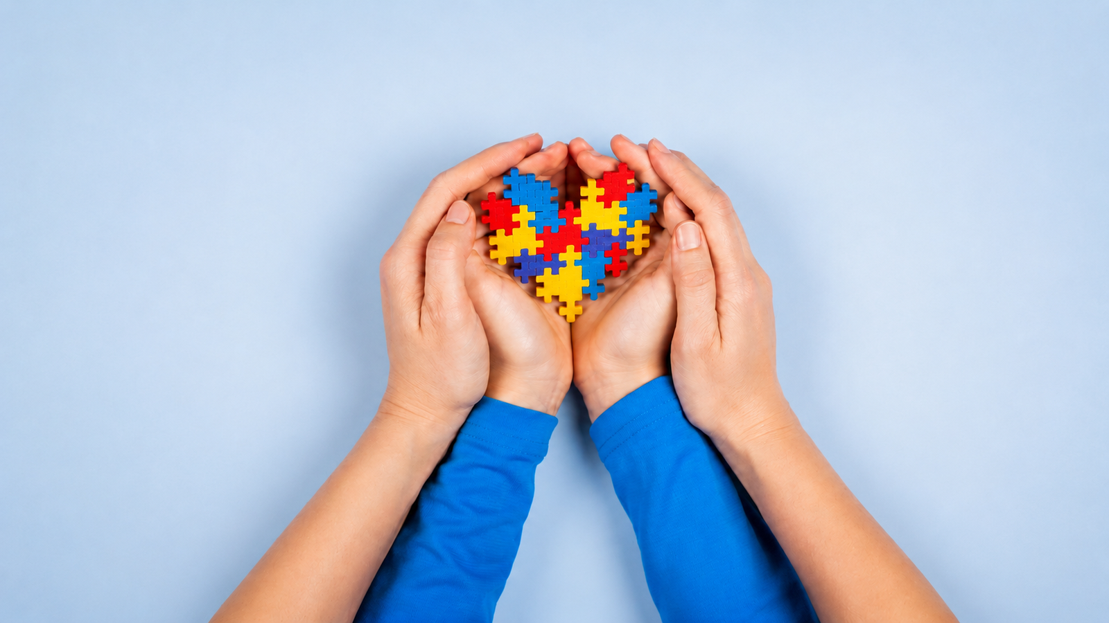 Hands protecting a colorful heart symbolizing autism acceptance and support